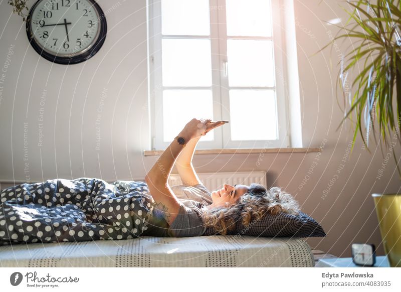 Junge Frau benutzt Smartphone im Bett Morgen Uhr aussruhen Erholung schlafen wach Wecker schläfrig Aufwachen Appartement Freizeit Schlafzimmer Haus heimwärts