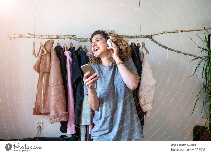 Junge Frau hört Musik in ihrem Schlafzimmer Mode Bekleidung Kleidung modisch Ablage auserwählend Einzelhandel Laden Werkstatt Sale Kleiderbügel Kunde Stil