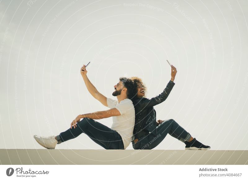 Glückliches Paar nimmt Selfies an der Wand Smartphones Sitzen Rücken an Rücken Großstadt Termin & Datum jung modern Straße Mann Frau Zusammensein romantisch
