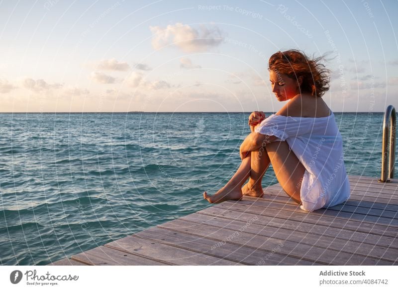 Junge Frau auf Pier in der Nähe von Meer MEER Sitzen Lächeln Himmel Wolken Abend Malediven sinnlich jung Resort Urlaub Paradies Freiheit sorgenfrei Lifestyle