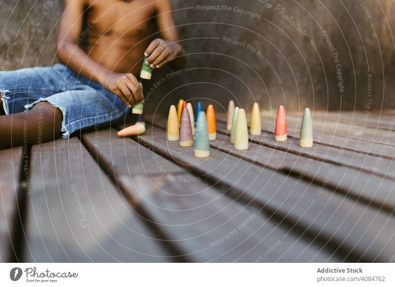 Crop schwarzes Kind spielt mit Kegeln Junge Spielen Sitzen sonnig tagsüber ohne Hemd farbenfroh Lifestyle Freizeit ruhen sich[Akk] entspannen Afroamerikaner