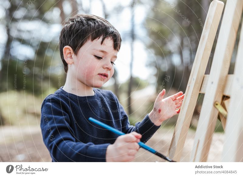 Junge malt auf Staffelei in der Landschaft Malerei Leinwand Kunst Pinselblume Kind kreativ rot Freizeit Lifestyle abstrakt niedlich bezaubernd süß Sitzen Farbe
