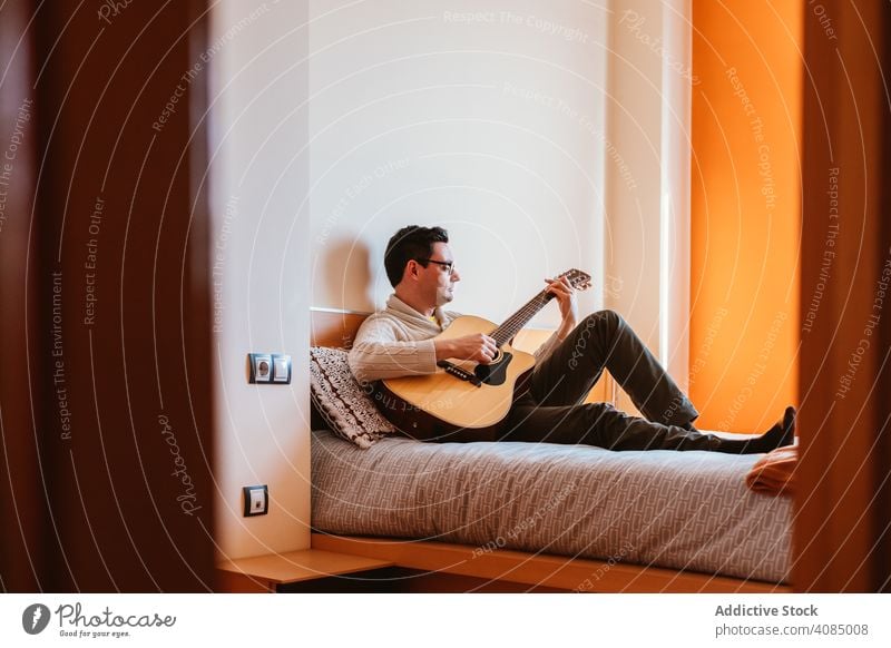 Mann spielt die Gitarre auf dem Bett Spielen Musik Sitzen heimwärts Schlafzimmer Person männlich Instrument Musiker spielen jung Menschen Kaukasier benutzend