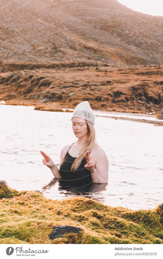 Frau mit Hut meditiert im Wasser in der Nähe von Steinufer meditierend Ufer geschlossene Augen Badeanzug kalt Oberfläche Küste Felsen Erholung jung Natur Yoga