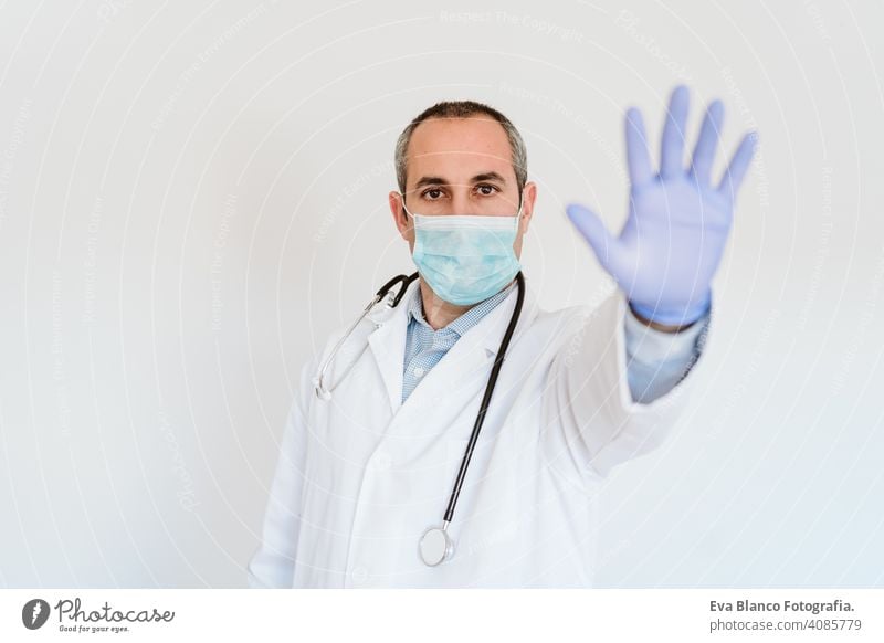 Porträt eines Arztes mit Schutzmaske und Handschuhen in einem Raum. Macht ein Stoppschild mit der Hand. Corona-Virus-Konzept stoppen Mann professionell