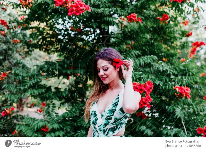 Porträt der schönen blonden jungen Frau lächelnd bei Sonnenuntergang. Spielend mit roten Blumen. Glück und Lifestyle-Konzept im Freien Kaukasier zahnfarben