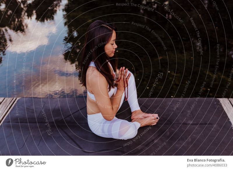 junge schöne asiatische Frau macht Yoga in einem Park. Sitzen auf der Brücke mit Reflexion auf dem Wasser See. Yoga und gesunder Lebensstil Konzept praktizieren