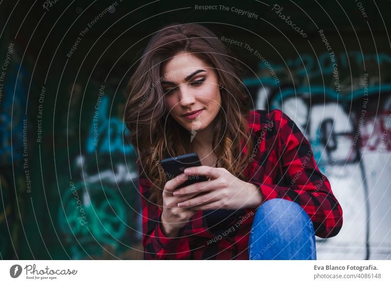 Junge schöne Frau, die ein Mobiltelefon benutzt. Urban Graffiti Hintergrund. Im Freien Lebensstil.Technologie urban Hut Stehen attraktiv Mobile Zaun Stadtbild