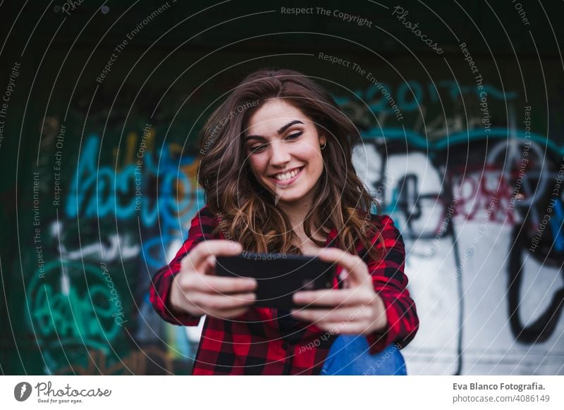 Junge schöne Frau, die ein Mobiltelefon benutzt. Sie macht ein Foto. Urban Graffiti Hintergrund. Im Freien Lebensstil.Technologie urban Hut Stehen attraktiv