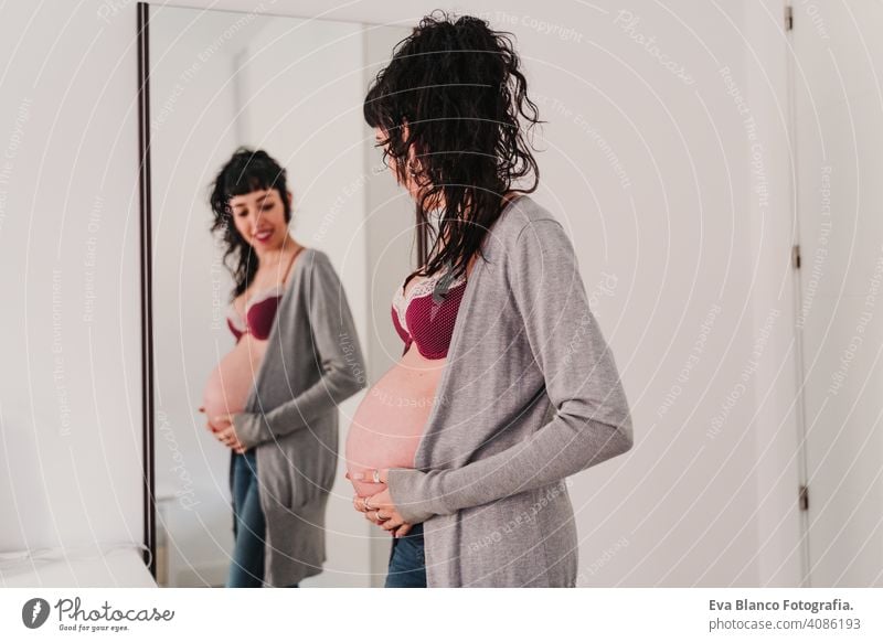Porträt einer jungen schwangeren Frau zu Hause, die in den Spiegel schaut heimwärts Lifestyle erwartend Fenster tagsüber Leben Erwartung Schönheit