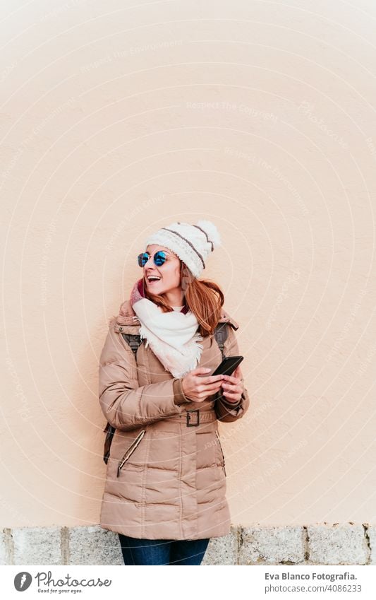 Frau mit Mobiltelefon über gelbe Wand Hintergrund. Technologie und Winter Konzept im Freien Großstadt Handy Technik & Technologie Lebensstile Sonnenbrille