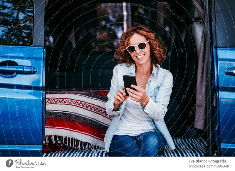 glückliche Frau, die in einem blauen Van sitzt und Spaß hat. Reisekonzept. Frau benutzt Mobiltelefon Glück Lachen Kleintransporter PKW reisen Handy genießend