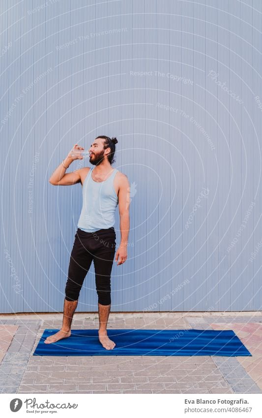 Mann in der Stadt übt Yoga Sport und Trinkwasser. blauen Hintergrund. gesunden Lebensstil Gesundheit im Freien Großstadt Blauer Hintergrund muskulös jung