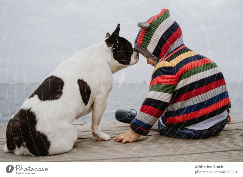 Anonymes Kind streichelt Hund auf Pier tätscheln Haustier MEER Sitzen gehorsam Baby französische Bulldogge lässig Lifestyle Freizeit ruhen sich[Akk] entspannen