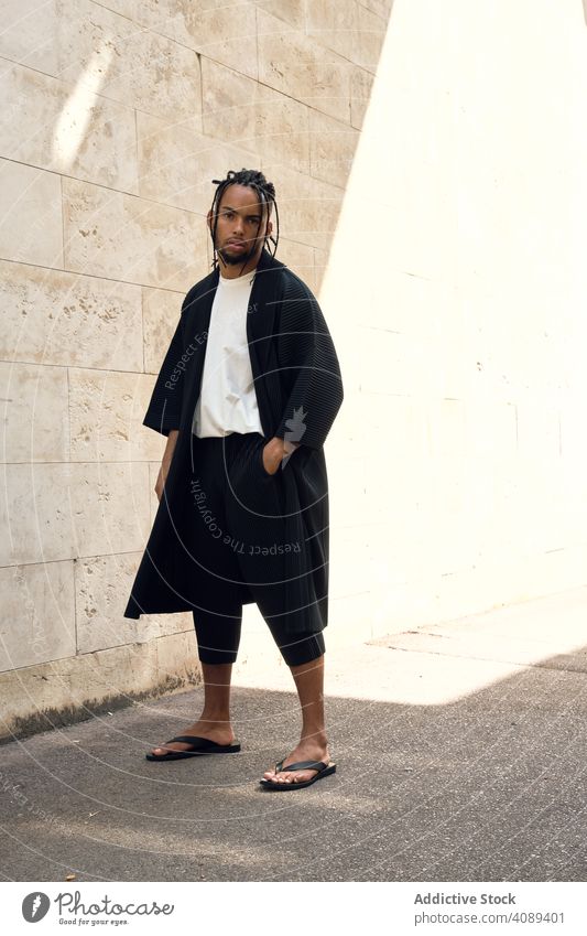 Entspannter schwarzer Kerl auf der Straße Mann entspannt Wand Hände in den Taschen Afroamerikaner Großstadt jung stylisch sonnig tagsüber männlich Lifestyle