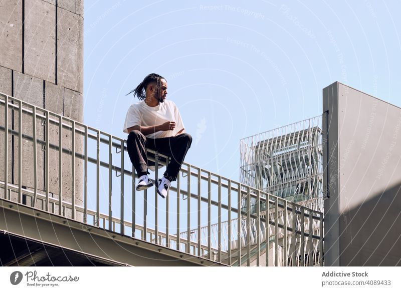 Schwarzer Mann sitzt auf Brücke Großstadt Straße Sitzen Reling Afroamerikaner urban sonnig tagsüber männlich jung lässig Lifestyle Freizeit ruhen