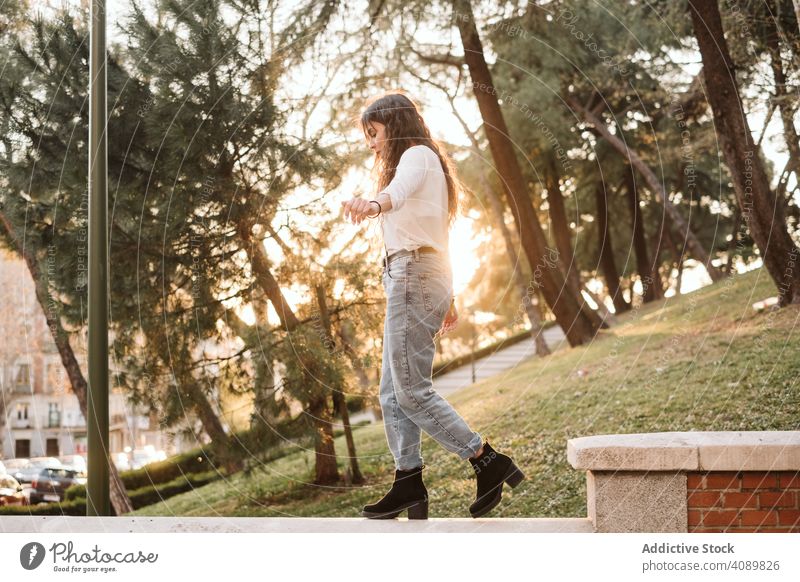 Junge Frau spaziert auf der Grenze im Park Borte Gleichgewicht laufen ausgestreckte Arme sonnig tagsüber jung lässig fokussiert konzentriert Lifestyle Freizeit
