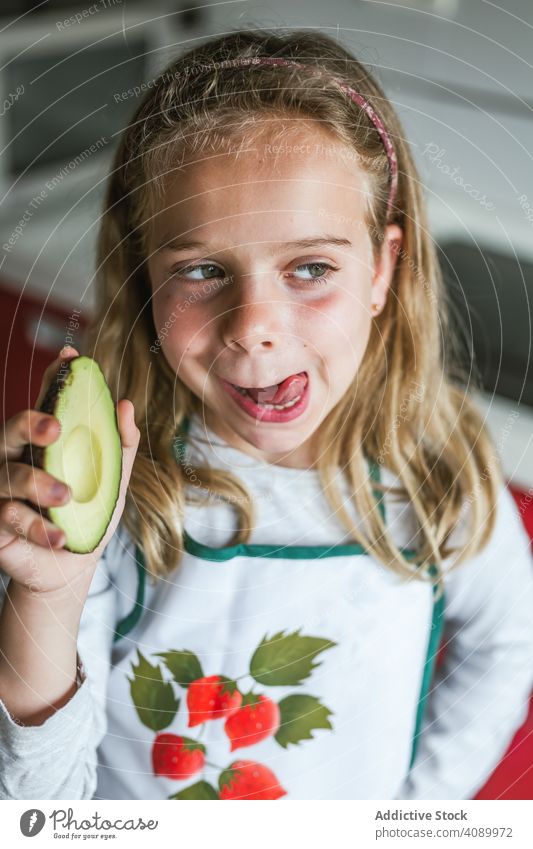 Mädchen mit Avocado lecken Lippen Küche Lippen lecken geschmackvoll frisch Vitamin Kind heimwärts Wegsehen Schürze Lebensmittel Essen zubereiten lecker Gesicht