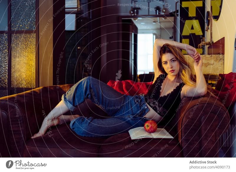 Junge sexy Frau sitzt auf Sofa mit Apfel Buch posierend Hand auf Kopf Liege jung schön attraktiv hübsch charmant sinnlich cool verführerisch traumhaft einladend