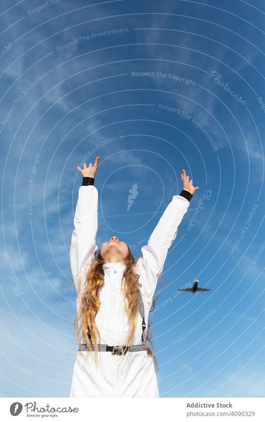 Fröhlicher Teenager versucht, fliegendes Flugzeug zu erreichen Mädchen Ebene erreichend Hände hoch Lächeln Himmel Wolken sonnig tagsüber Glück aufgeregt heiter