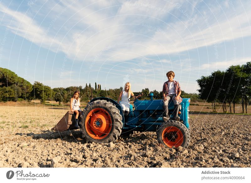 Gruppe junger Freunde, die auf einem blauen Traktor in einem ländlichen Gelände sitzen und in die Kamera schauen Bauernhof Enkel Feld Reiten Zusammensein sonnig