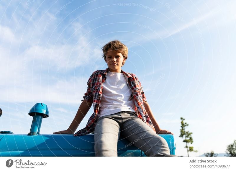 Junge sitzt auf Traktor auf Bauernhof Feld Ackerbau Himmel Wolken sonnig tagsüber Sitzen Teenager Kind lässig Lifestyle Freizeit sich[Akk] entspannen ruhen