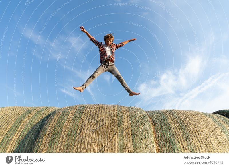 Barfuß Junge springen auf Heuhaufen Bauernhof Himmel Wolken sonnig tagsüber Natur Lifestyle Freizeit Teenager Kind getrocknet Gras Stroh Brötchen Landschaft