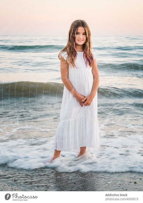 Lächelndes Mädchen steht am Meer zwischen Wellen Porträt Seeküste winken charmant Wasser Strand bezaubernd Stehen Sommer schön Frau Kind Kindheit Vorschulkind