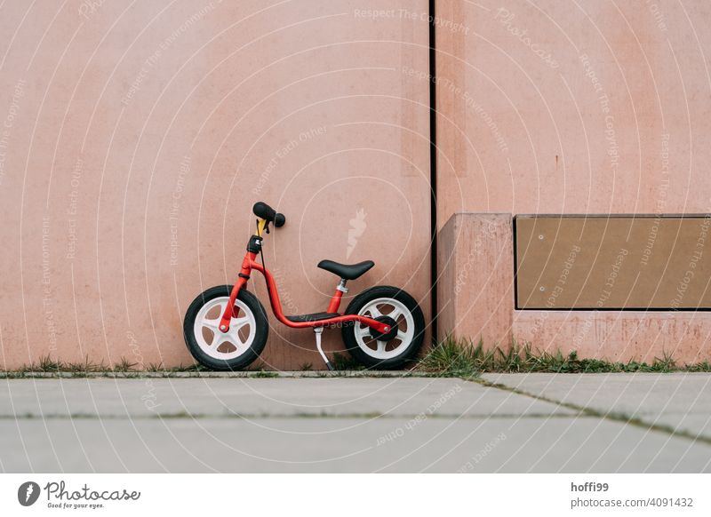 ein rotes Laufrad, geparkt vor rosa Wand Kinderrad minimalistisch kinderlaufrad Fahrrad Fahrradfahren Kindheit Rad Lifestyle Bewegung Verkehrsmittel Mobilität