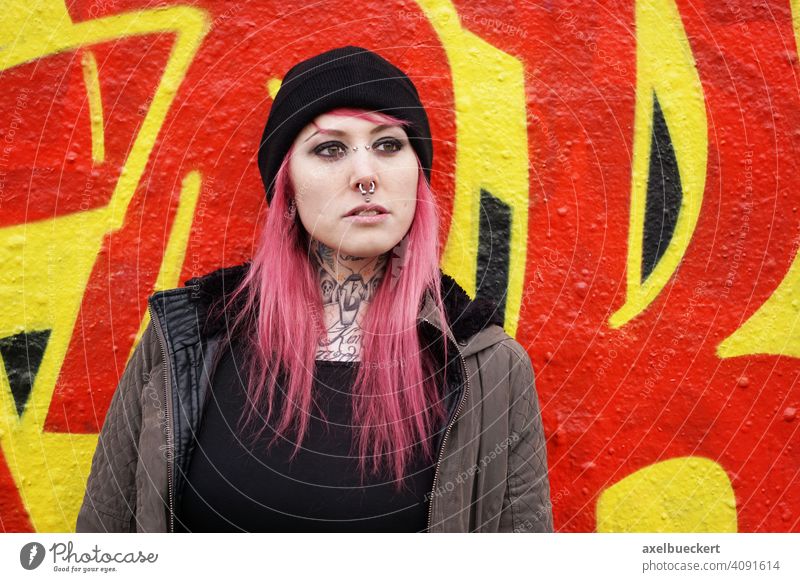 junge Frau mit pinken Haaren, Piercings und Tattoos vor Graffiti-Wand Junge Frau E-Girl Hipster echte Menschen Subkultur pinke haare gepierct tätowiert