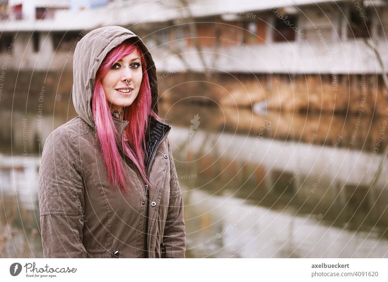 junge Frau mit pinken Haaren, Piercings und Tattoos vor Graffiti beschmierten Häusern Junge Frau echte Menschen Subkultur pinke haare gepierct tätowiert