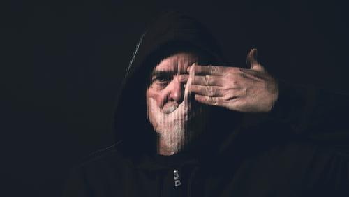 Porträt eines Mannes mit Kapuzenpulli, der eine Hand vor sein Gesicht hält alt Vollbart verdoppeln Belichtung streifen Hände Auge Mund stumm blind Atelier