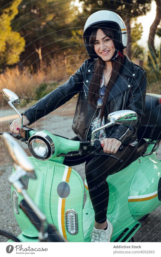 Frau in Motorradhelmen sitzt auf dem Fahrrad und schaut in die Kamera attraktiv Schutzhelm Tretroller Aktivität Freizeit Straße heiter Abenteuer reisen
