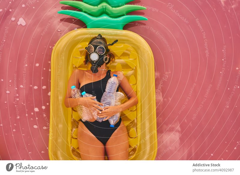 Weiblich mit Gasmaske und mit Plastikflaschen im Seewasser Frau Umwelt Kunststoff MEER Atemschutzgerät Müll Luftmatratze Konzept sozial rosa Badeanzug