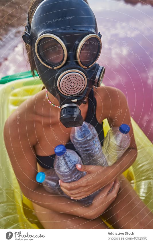 Weiblich mit Gasmaske und mit Plastikflaschen im Seewasser Frau Umwelt Kunststoff MEER Atemschutzgerät Müll Luftmatratze Konzept sozial rosa Badeanzug