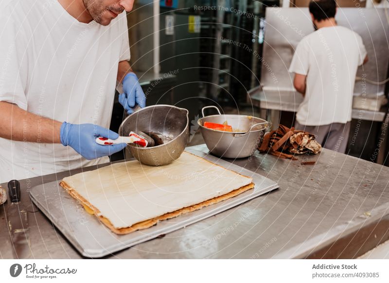 Crop-Konditor schmiert Marmelade auf Croissant Bäckerei Arbeit Schliere Werkzeug Abfertigungsschalter Küche Koch Vorbereitung Hygiene süß Brötchen Gebäck