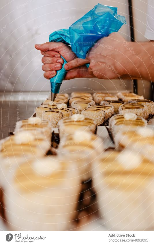 Anonymer Bäcker beim Verzieren von Gebäck mit Sahne Konditor Bäckerei drücken Dekor Tasche Qualität Lebensmittel Mann Kleinunternehmen Arbeit Job geschmackvoll