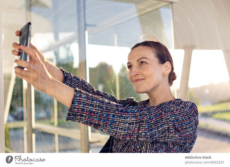 Lächelnde Geschäftsfrau nimmt Selfie auf der Straße Smartphone Gebäude Büro Eingang modern Großstadt urban Frau heiter Arbeit Wand Glas Job Telefon Mobile Gerät