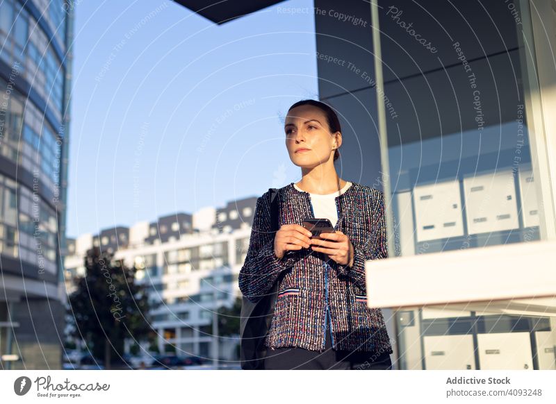 Lächelnde Geschäftsfrau beim Telefonieren mit dem Handy Smartphone Gebäude Büro Eingang Straße modern Großstadt urban Frau heiter Arbeit Wand Glas Job Mobile