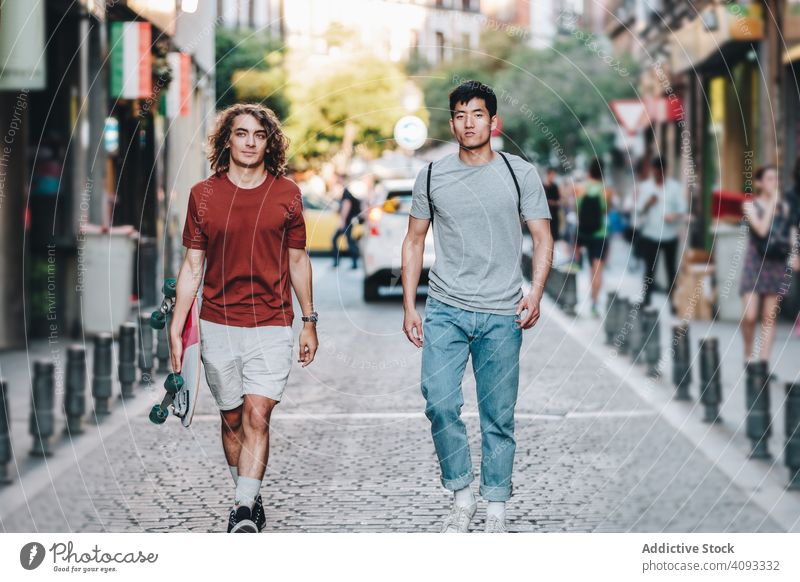 Coole multirassische männliche Freunde unterhalten sich beim Gehen auf der Straße mit Longboard Talkrunde Spaziergang lässig entspannt interessiert sorgenfrei
