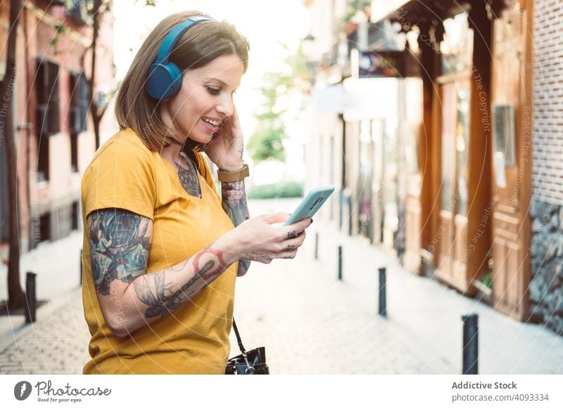 Inspirierte Frau mit Kopfhörern, die auf der Straße mit ihrem Smartphone Musik hört Hipster zuhören cool benutzend Streaming Drahtlos achtsam inspiriert