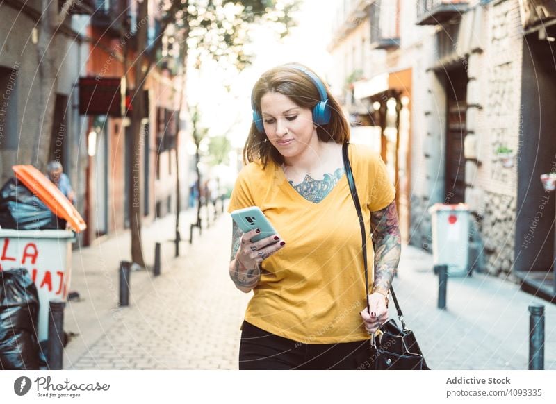 Inspirierte Frau mit Kopfhörern, die auf der Straße mit ihrem Smartphone Musik hört Hipster zuhören cool benutzend Streaming Drahtlos achtsam inspiriert