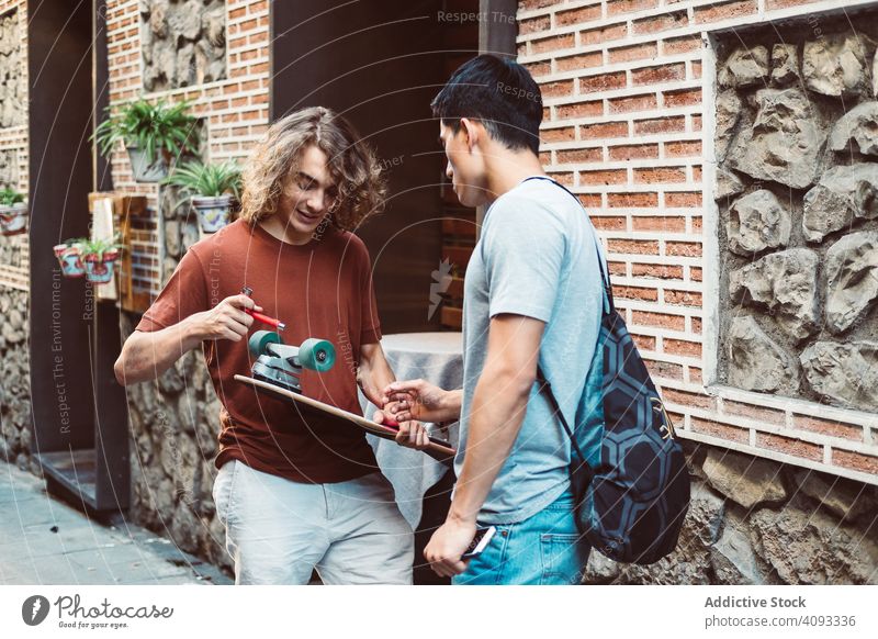 Interessierter männlicher Freund diskutiert über Longboard, während er auf der Straße steht Besprechung teilen reden achtsam lässig Männer urban Gebäude