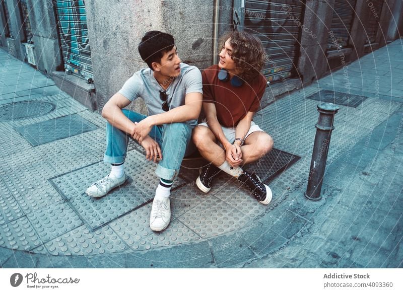 Entspannte multirassische männliche Freunde unterhalten sich, während sie sich an einer Gebäudeecke auf der Straße ausruhen reden positiv entspannt