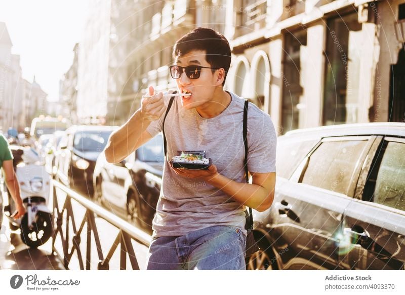 Mann isst Essen zum Mitnehmen auf einer Straße in der Stadt Imbissbude Essstäbchen Straßenessen hungrig Großstadt Asiatische Küche urban sonnig Imbisswagen