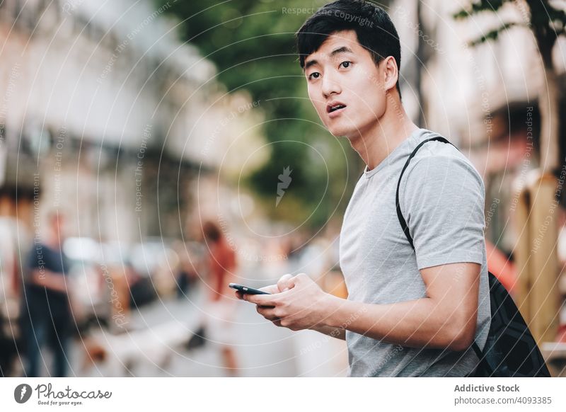 Verwirrter asiatischer Mann benutzt sein Smartphone, während er auf der Straße steht verwirrt benutzend Regie Browsen ungewiss lässig stehen verirrt erstaunt