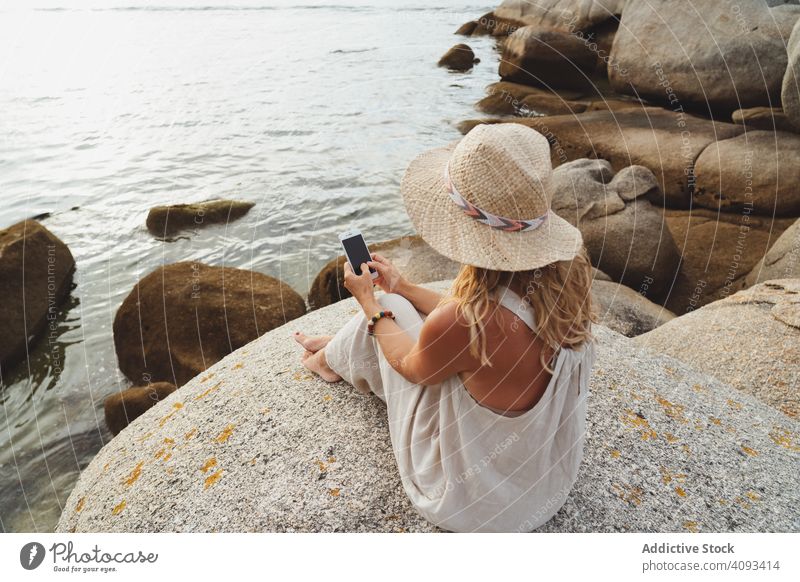 Zeitgenössische Frau mit Telefon, die am Meer chillt Meeresufer Smartphone Küste Kälte allein genießen Flucht reisen Seeküste Einsamkeit abgelegen Drahtlos
