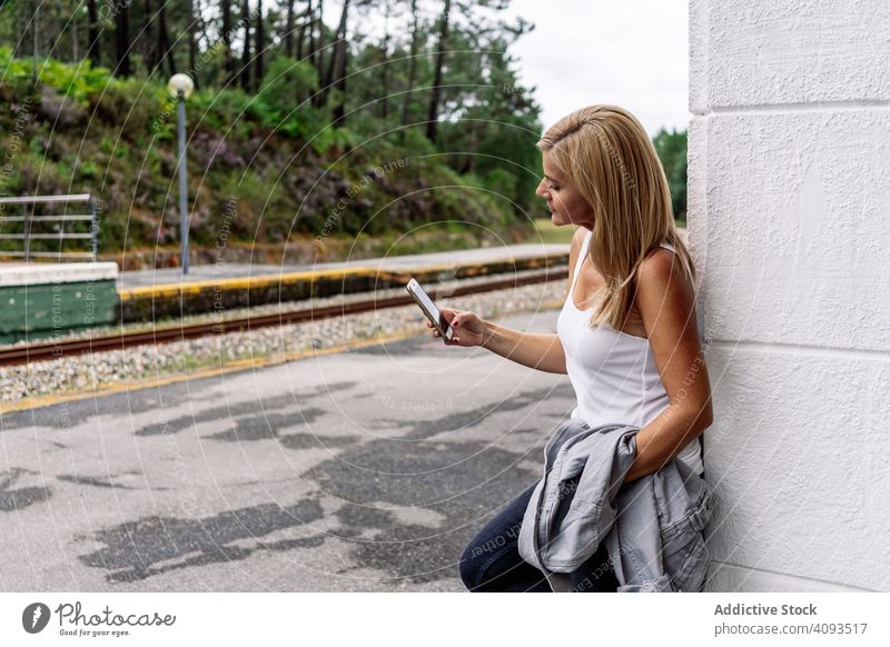 Zufriedene Frau auf dem Bahnhof mit Smartphone Eisenbahn Station benutzend zuschauend Browsen Podest Apparatur Gerät Surfen reisen Warten Tourist Reise online