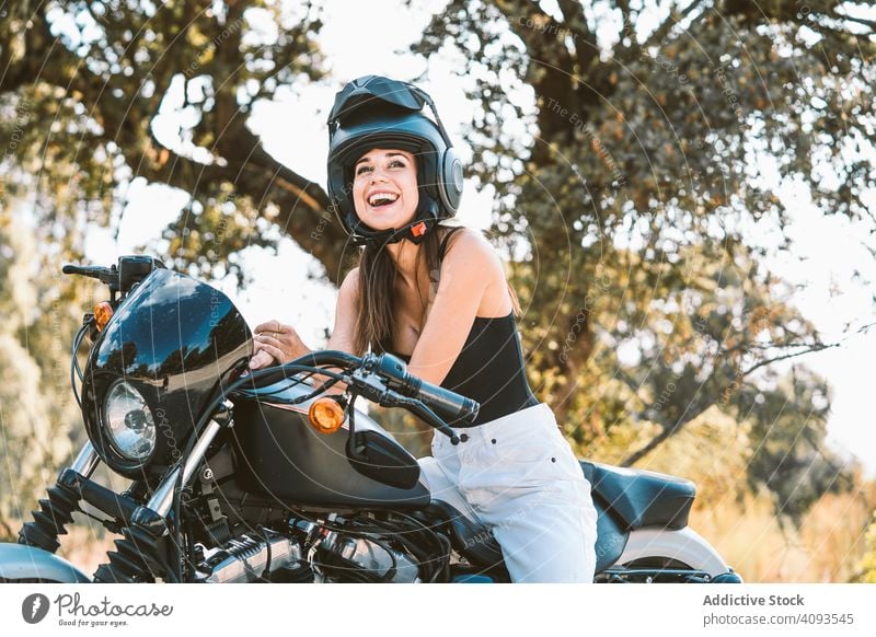 Aufmerksame Frau mit Helm sitzt auf einem geparkten Motorrad in einer ländlichen Gegend Schutzhelm cool sitzen selbstbewusst Freiheit ernst glänzend Sauberkeit