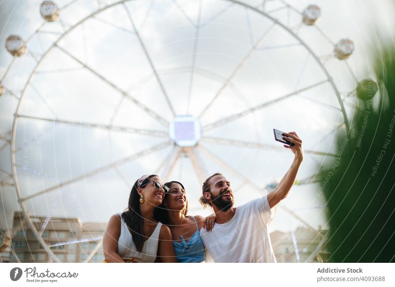 Sorglose Freunde machen ein Selfie mit ihrem Smartphone, während sie neben einem Karussell auf einem Jahrmarkt stehen sorgenfrei heiter Lächeln Spaß haben